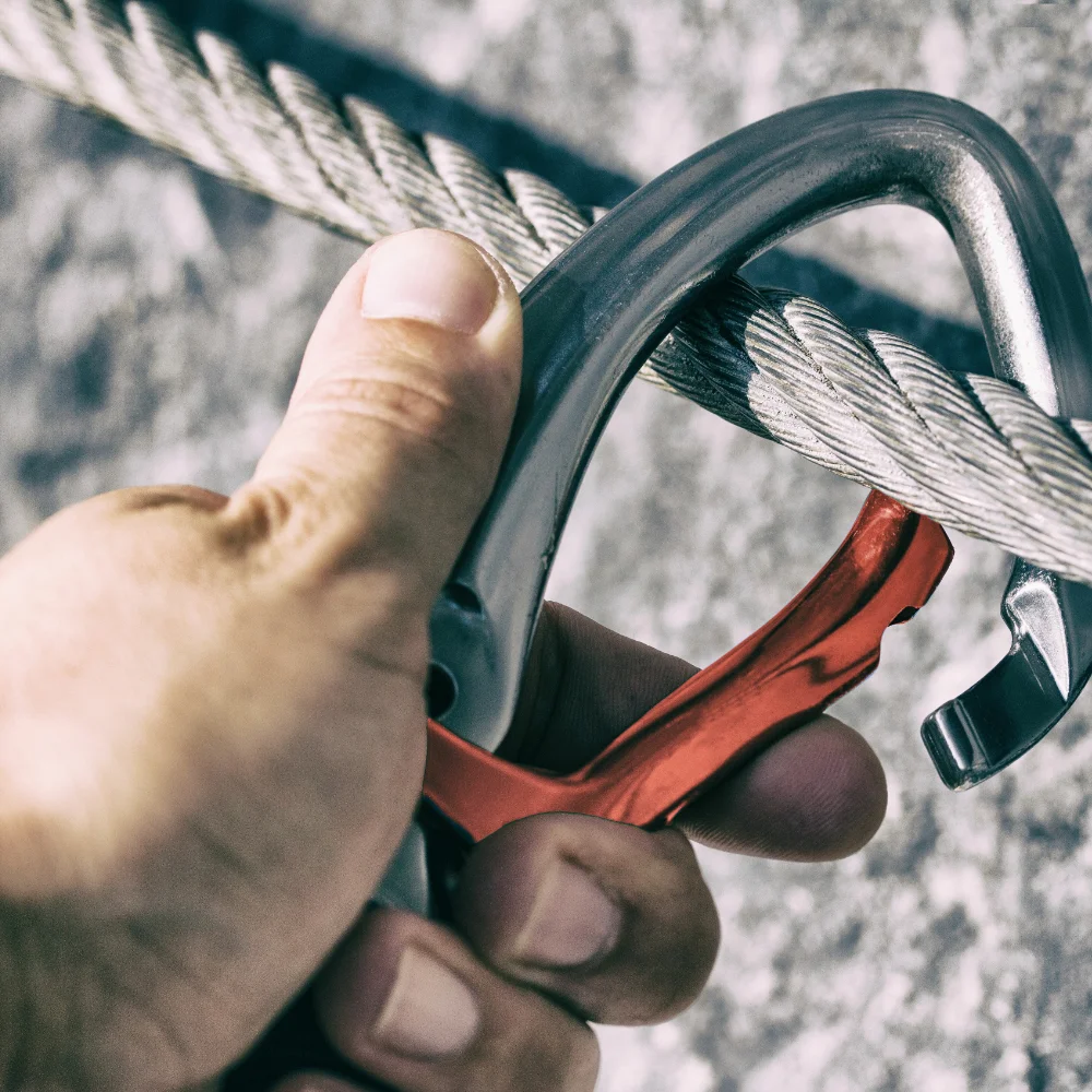 Eine Hand öffnet beim Klettern einen Karabiner an einer Seilsicherung.
